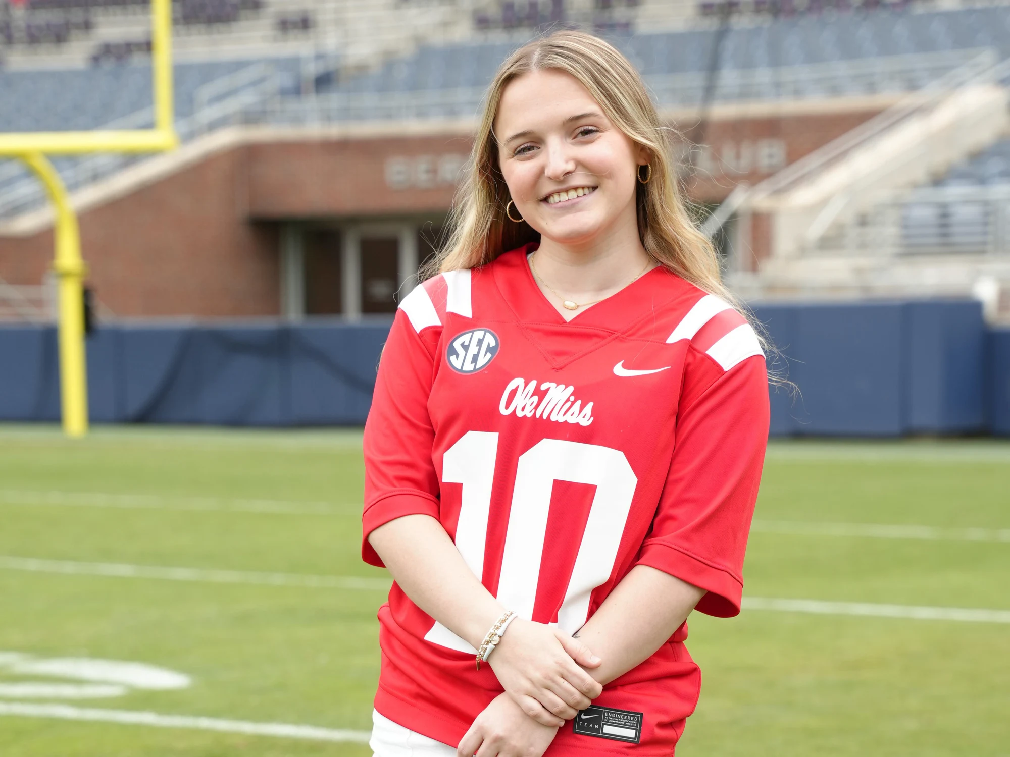 A smiling woman wearing a red sports jersey on a field.