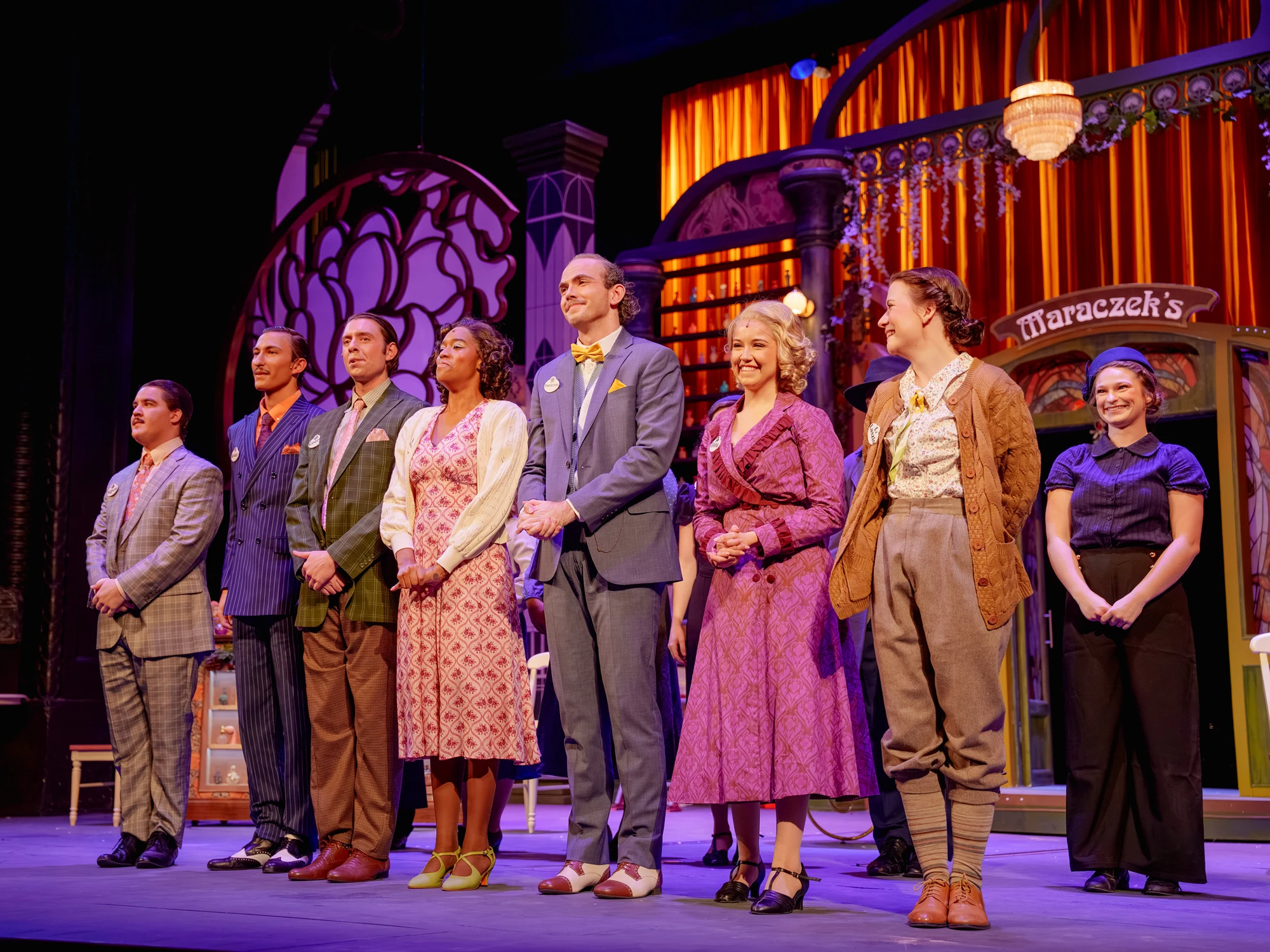 A theatre cast standing together on a brightly lit stage.